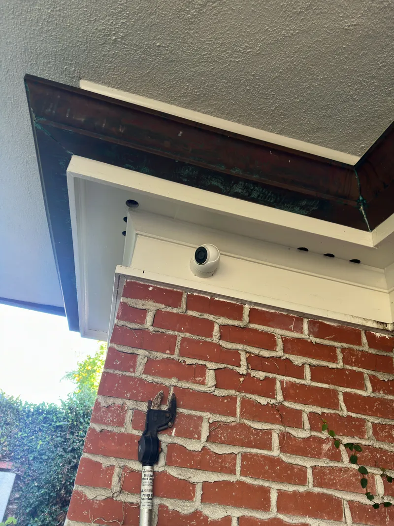 Small dome camera neatly mounted under a porch overhang above a brick wall