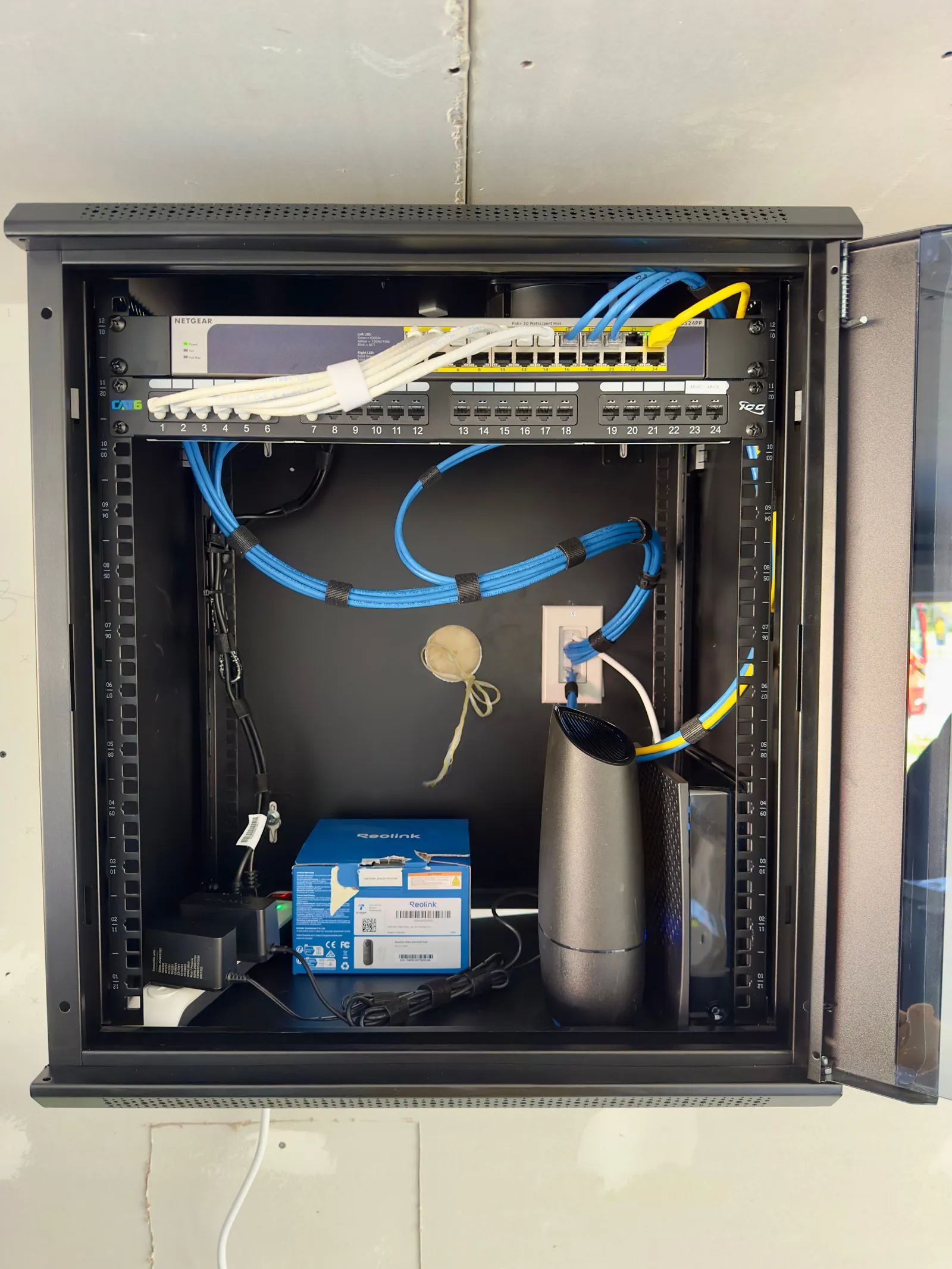 Wall-mounted home network rack with Cat6 patch panel, PoE switch, and neatly bundled cabling