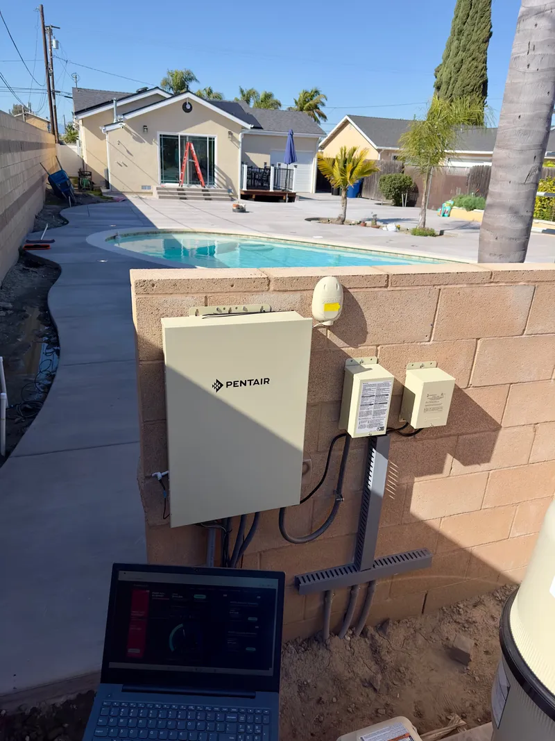 Pool automation control panel installed on a backyard block wall beside a pool